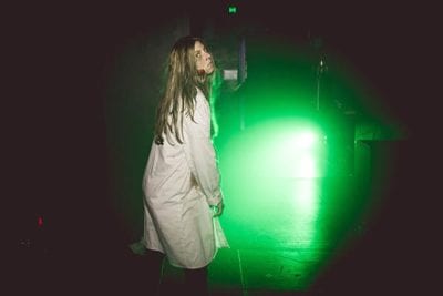 Zombie in lab coat in front of a bright green light