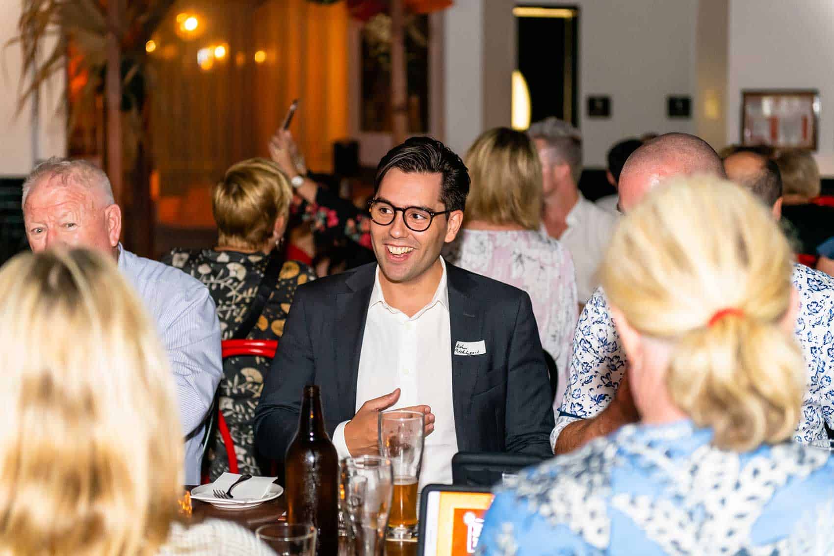 Man smiling sitting at a table during client appreciation event